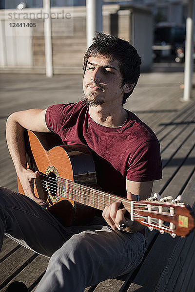 Young man sitting on a bench playing guitar