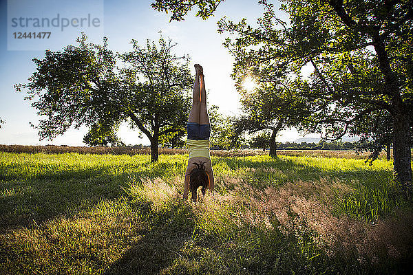 Young girl doing handstand on meadow at summer evening