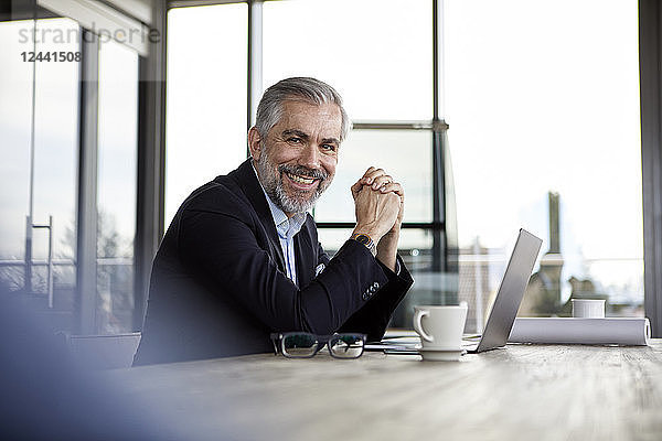 Portrait of smiling businessman with laptop at desk in office