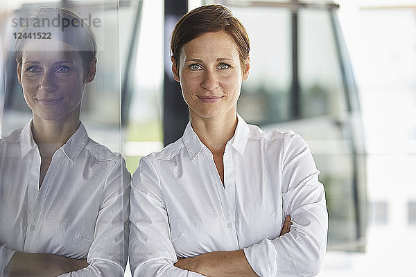 Portrait of smiling businesswoman leaning at glass pane in office
