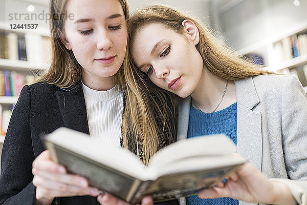 Portrait of two teenage girls reading booktogether in a public library