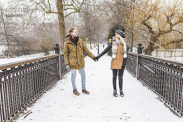 Young couple in love standing hand in hand on footbridge in a park on a snowy day