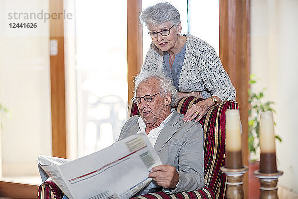 Senior man and woman sitting in library  reading newspaper