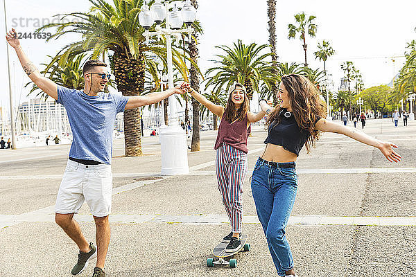 Carefree friends having fun with a skateboard on a promenade with palms