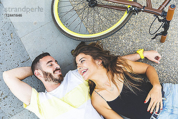 Happy couple lying on the ground next to bicycle and smiling at each other