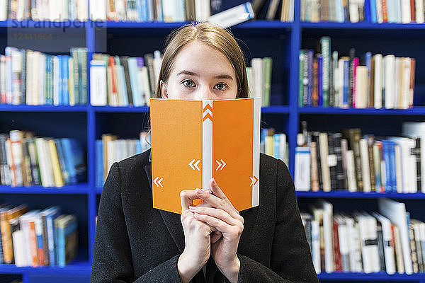 Teenage girl hiding behind book in a public library