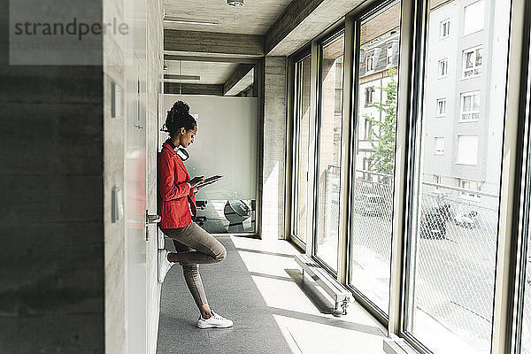 Young woman with headphones standing in corridor  using digital tablet