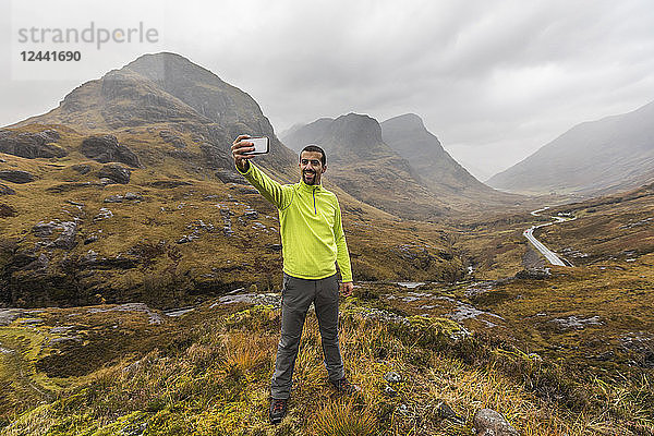 UK  Scotland  man in the Scottish highlands near Glencoe with a view on the Three Sisters taking a selfie