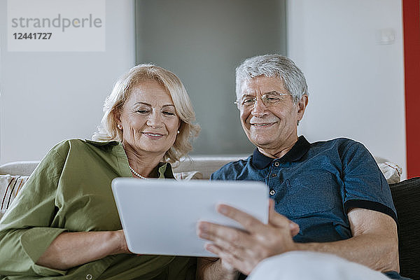 Senior couple at home sitting on couch sharing tablet
