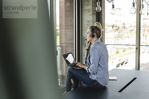 Young businesswoman sitting at desk  making a call  using headset and laptop