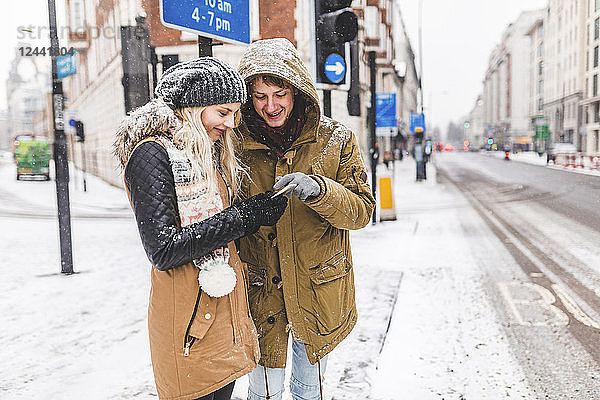 UK  London  young couple standing at roadside looking at cell phone on a snowy day