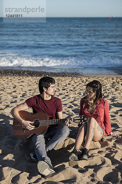 Couple with a guitar sitting on the beach