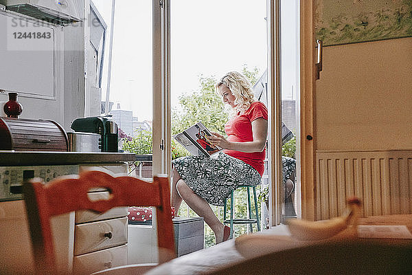 Pregnant woman sitting on balcony looking at photo book