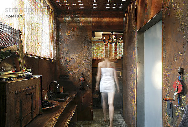 Back view of woman walking in bathroom with corten steel wall cladding and ceiling light effects