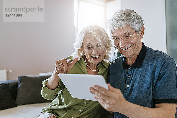 Happy senior couple at home sitting on couch sharing tablet