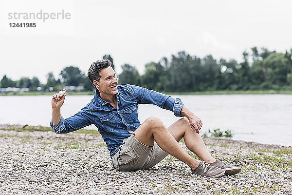 Laughing man sitting at the riverside throwing stones