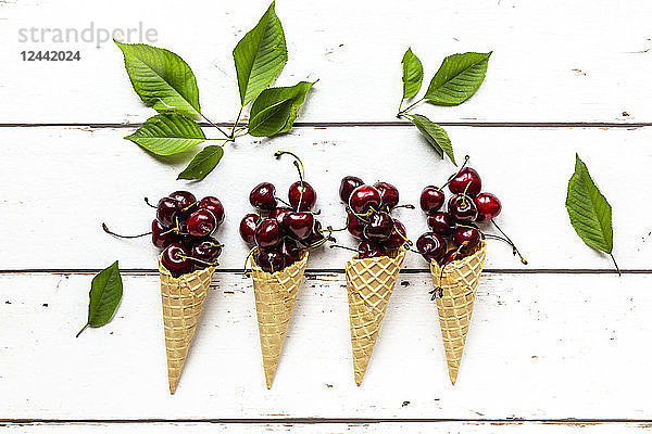 Row of four ice cream cones and cherries on white wood
