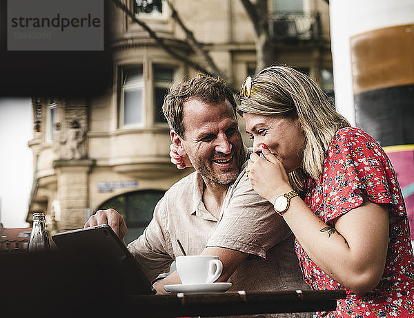 Happy couple with tablet at an outdoor cafe