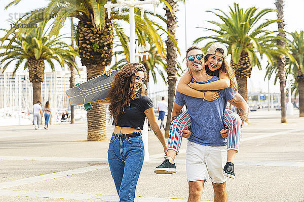 Happy friends with a skateboard walking on a promenade with palms