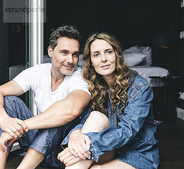 Smiling couple in nightwear at home sitting at French window