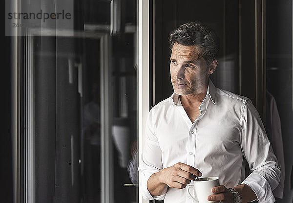 Businessman with cup of coffee looking out of window at home