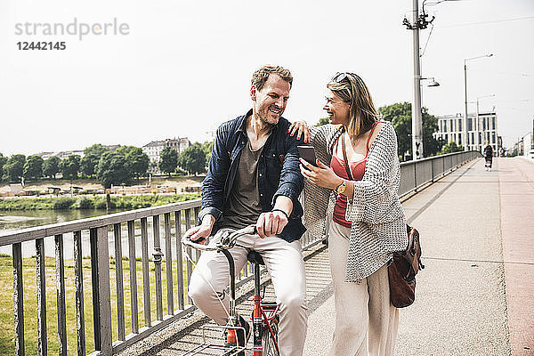 Happy couple with bicycle and cell phone crossing a bridge