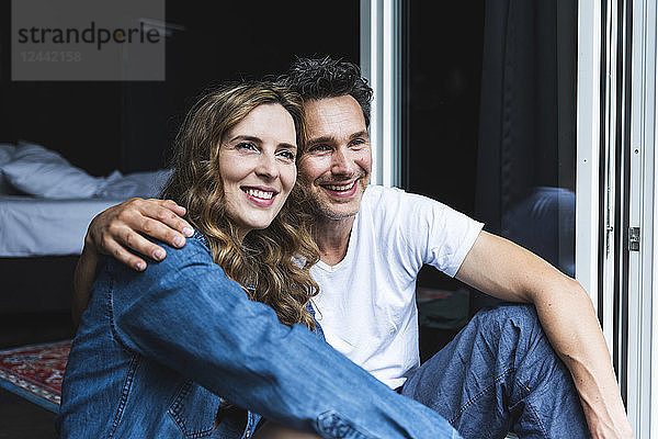 Happy couple in nightwear at home sitting at French window