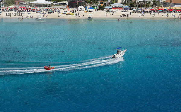 Motorboot  das einen aufblasbaren Sitz über das türkisfarbene Wasser des Karibischen Meeres vor einem belebten Strand zieht; Grand Turk Island  Turks- und Caicosinseln