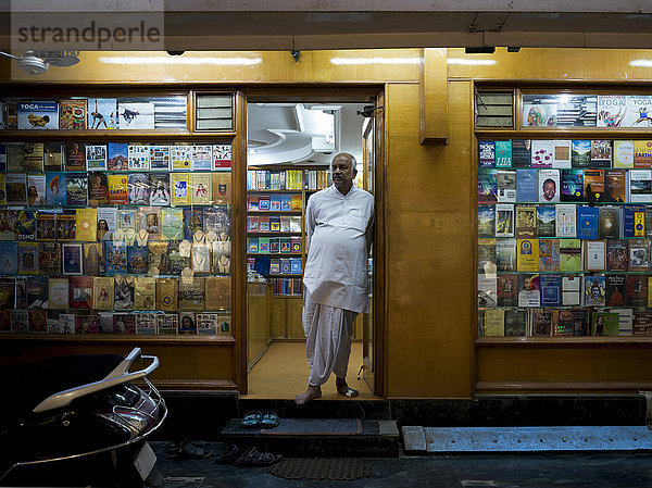 Ein männlicher Ladenbesitzer steht nachts in der Tür eines Buchladens; Rishikesh  Uttarakhand  Indien