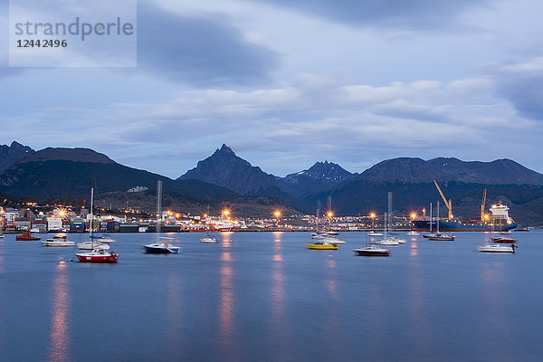 Hafenstadt in blauer Stunde mit anlegenden Booten und sich im Wasser spiegelnden Straßenlaternen; Ushuaia  Tierra del Fuego  Argentinien