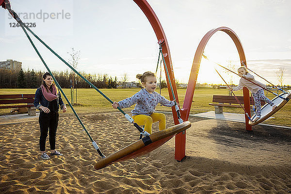 Eine junge Mutter und ihre Töchter spielen an einem warmen Herbstabend auf einer Untertassenschaukel auf einem Spielplatz; Edmonton  Alberta  Kanada