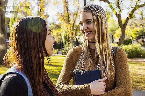 Zwei junge Studentinnen bleiben stehen und unterhalten sich  während sie über einen Universitätscampus gehen  Edmonton  Alberta  Kanada