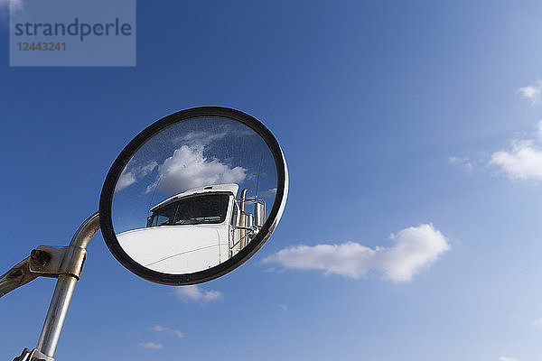 Ein Transport-LKW spiegelt sich im runden Seitenspiegel eines anderen LKW mit blauem Himmel  Minnesota  Vereinigte Staaten von Amerika