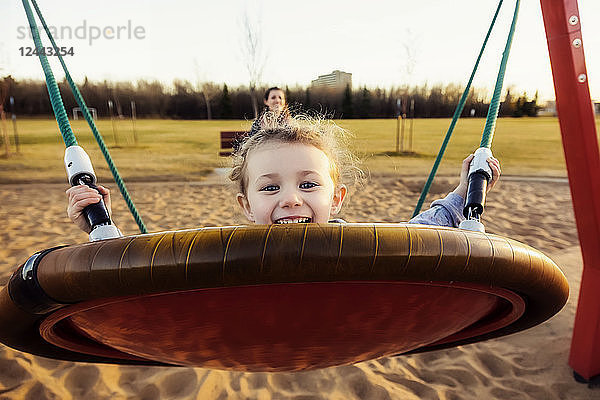 Eine junge Mutter und ihre Tochter spielen auf einer Untertassenschaukel auf einem Spielplatz an einem warmen Herbstabend; Edmonton  Alberta  Kanada