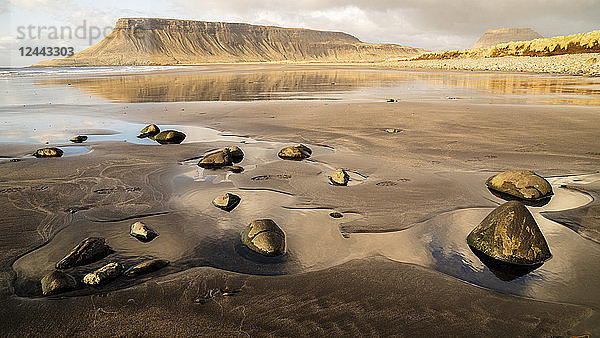 Felsen am nassen schwarzen Sandstrand entlang der isländischen Küste mit Klippen  die sich im Wasser spiegeln  in der Nähe von Kirkjufell; Grundarfjorour  Island