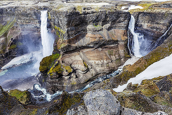 Die atemberaubenden erdigen Farben und Felsformationen zusammen mit dem ungeschmolzenen Schnee  der in der Talsohle des Haifoss zwischen zwei Wasserfällen ruht. Natürliche Schönheit an einem der großartigsten Aussichtspunkte für Wanderungen in Island  Island