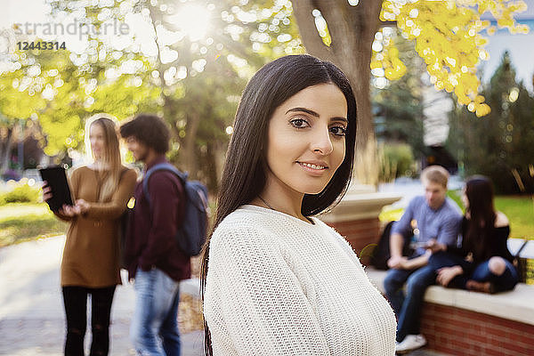 Eine junge Studentin libanesischer Abstammung posiert  während sich ihre Freunde im Hintergrund auf dem Universitätscampus unterhalten  Edmonton  Alberta  Kanada
