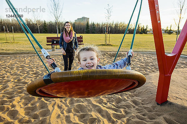 Eine junge Mutter und ihre Tochter spielen auf einer Untertassenschaukel auf einem Spielplatz an einem warmen Herbstabend; Edmonton  Alberta  Kanada