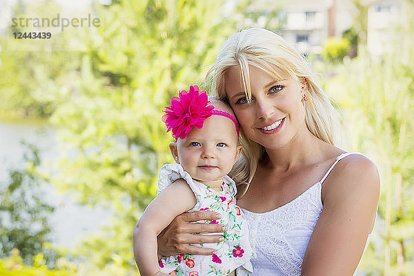 Eine hübsche junge Mutter mit langen blonden Haaren genießt die Zeit mit ihrer süßen kleinen Tochter in einem Stadtpark an einem Sommertag und posiert für die Kamera  Edmonton  Alberta  Kanada
