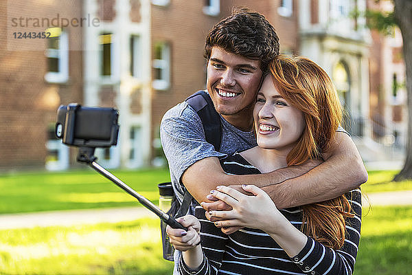 Ein junges Paar steht zusammen auf dem Universitätsgelände und macht ein Selfie mit einem Smartphone an einem Selfie-Stick  Edmonton  Alberta  Kanada