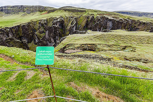 Ein Schild mit der Aufschrift Keep out Flora Protected Area (Flora-Schutzgebiet) in Englisch und Isländisch steht an einem Zaun an einem touristischen Standort in Fjadrargljufur  Island.