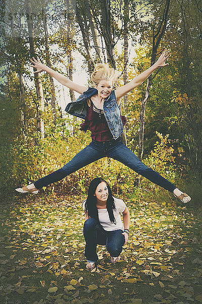 Eine junge Frau springt hoch in die Luft über ihre Freundin in einem Park während der Herbstsaison  Edmonton  Alberta  Kanada