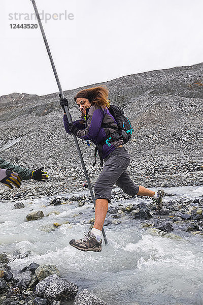 Eine Frau springt mit Hilfe einer Stange über einen reißenden Gletscherbach in der Nähe des Gulkana-Gletschers  Alaska  Vereinigte Staaten von Amerika