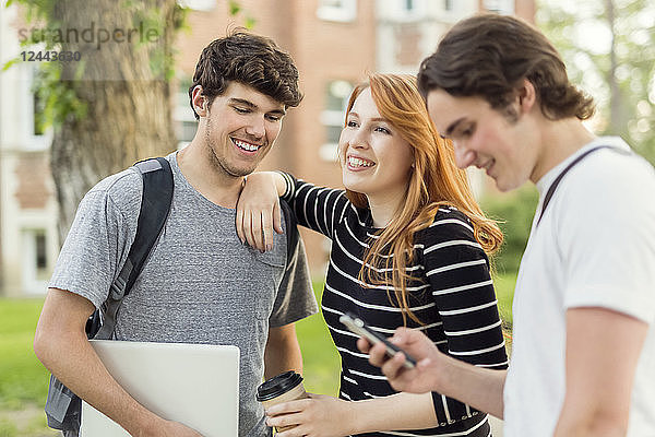 Drei Freunde stehen auf dem Universitätscampus und unterhalten sich mit ihrem Smartphone und Laptop  Edmonton  Alberta  Kanada