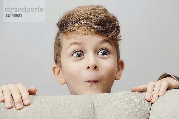 Porträt eines kleinen Jungen  der mit einem albernen  weit aufgerissenen Gesichtsausdruck hinter einer Couch hervorschaut; Langley  British Columbia  Kanada