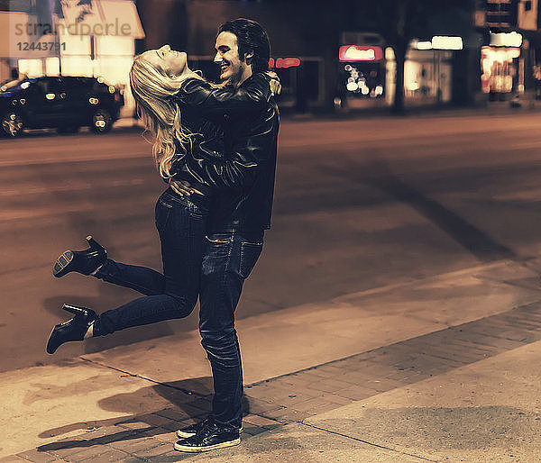 Ein junges Paar in schwarzen Lederjacken  das nachts auf einem Bürgersteig in der Stadt spielt  Edmonton  Alberta  Kanada