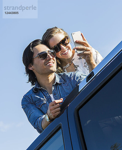 Ein junges Paar steht durch das Schiebedach seines Autos auf und macht ein Selbstporträt mit seinem Handy  Edmonton  Alberta  Kanada