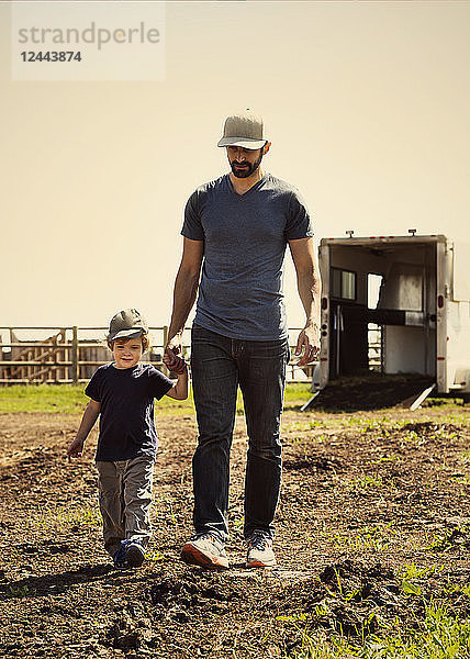 Ein Vater geht mit seinem kleinen Sohn auf einem Bauernhof spazieren und hält ihn an der Hand  Edmonton  Alberta  Kanada