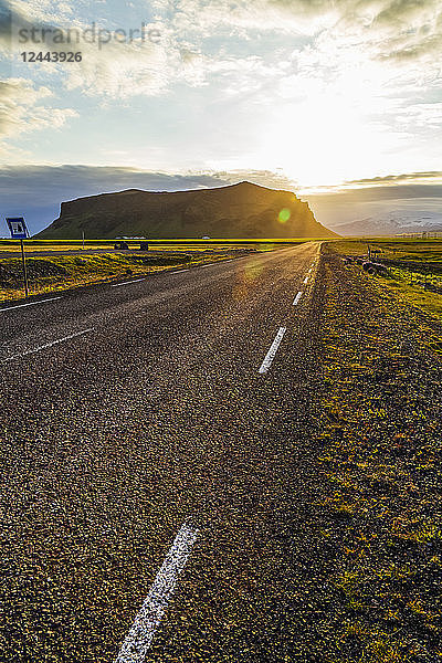 Die Sonne geht hinter den Hügeln unter  eine asphaltierte Straße führt in den Sonnenuntergang  Island