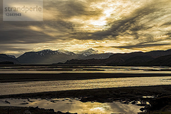 Die Sonne geht am späten Abend kurz vor der Sommersonnenwende unter und zeichnet die Silhouette der Berge und des Flusses in dieser abgelegenen Landschaft  Island